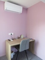 Una habitación pequeña y ordenada con un escritorio, una silla y un aire acondicionado instalado en la pared.