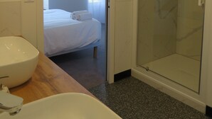 A modern bathroom with a large white bathtub, a glass shower enclosure, and a bed visible through an open door. - Les Jardins de Saulzet (Romagnat)