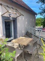 Un espacio al aire libre con mesa y sillas, un porche cubierto y vista a un estacionamiento.