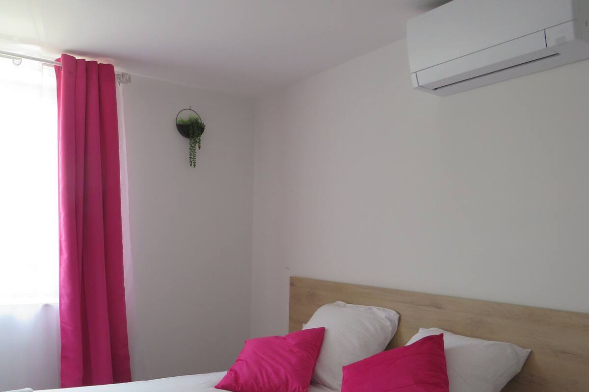 A hotel room with a large bed, white bedding, and two pink pillows.
