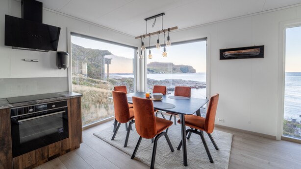 A modern kitchen with a built-in oven and a dining area with a table and chairs. - Runde Panorama - Østen Pilot (Heroy)