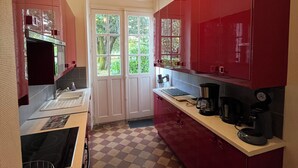 Een kleine keuken met rode kastjes, een geruit vloertje en een hangende lamp.