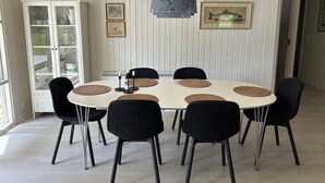Un coin repas avec une table ronde, des chaises noires, des sets de table en fibres tressées et des œuvres d’art encadrées accrochées aux murs.