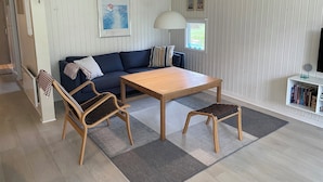 Une pièce comprenant un canapé, une table en bois, un banc, une lampe, un tableau au mur et une bibliothèque.