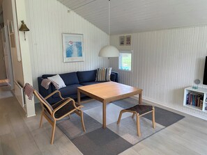 Una habitación con sofá, una mesa de madera, un banco, una lámpara, un cuadro en la pared y una estantería.