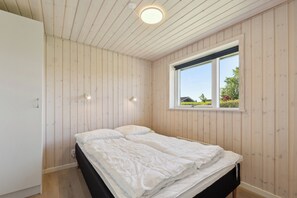 A bedroom with wooden walls, a window with a view, and a bed with white bedding.