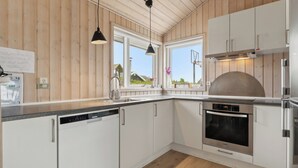 A modern kitchen with wooden walls, white cabinets, a dishwasher, an oven, and pendant lighting. - Activity house - Flovt Strand, Haderslev (Haderslev)