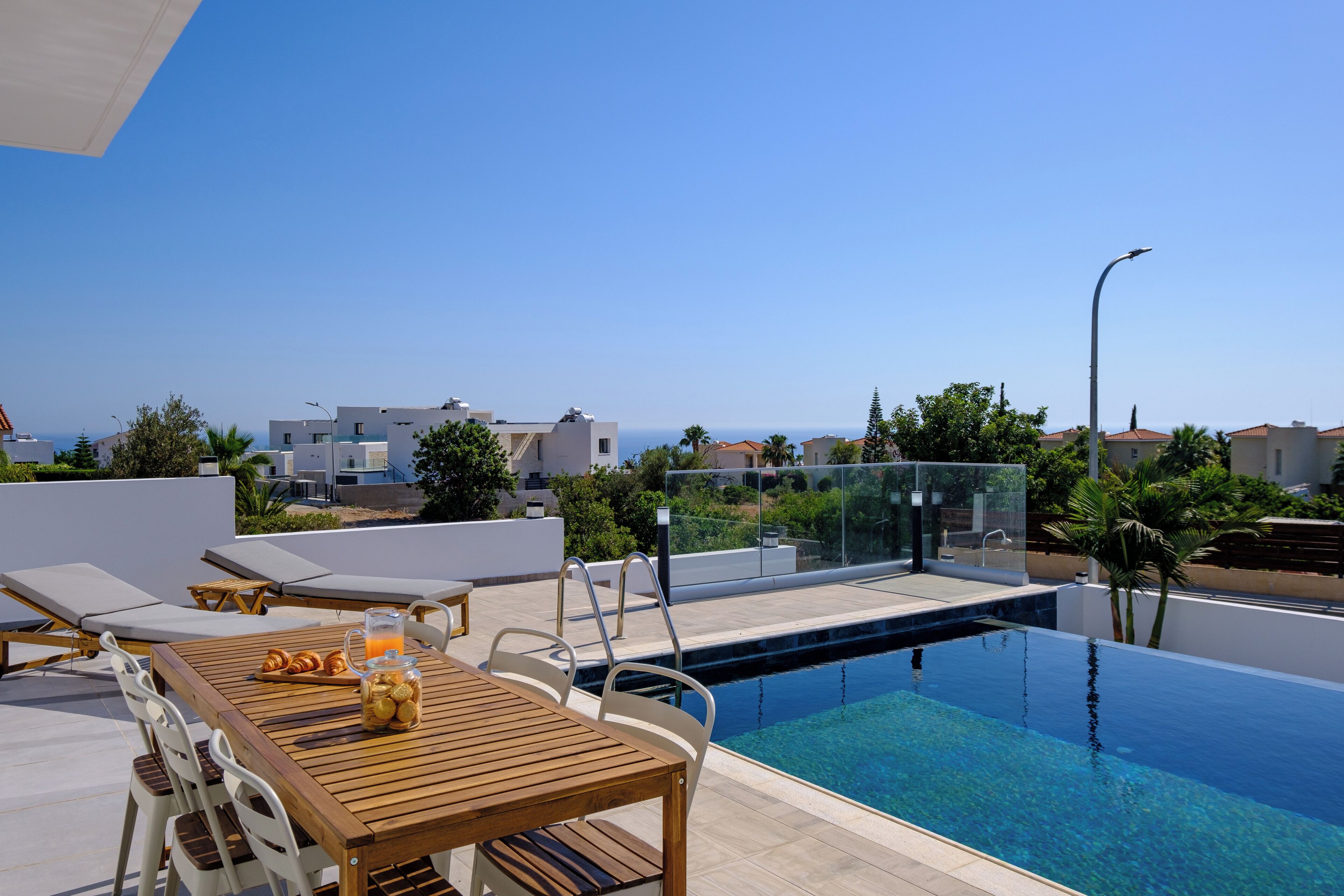 Un espace piscine aménagé sur le toit, avec une table en bois, des chaises longues et une vue dégagée sur la mer.