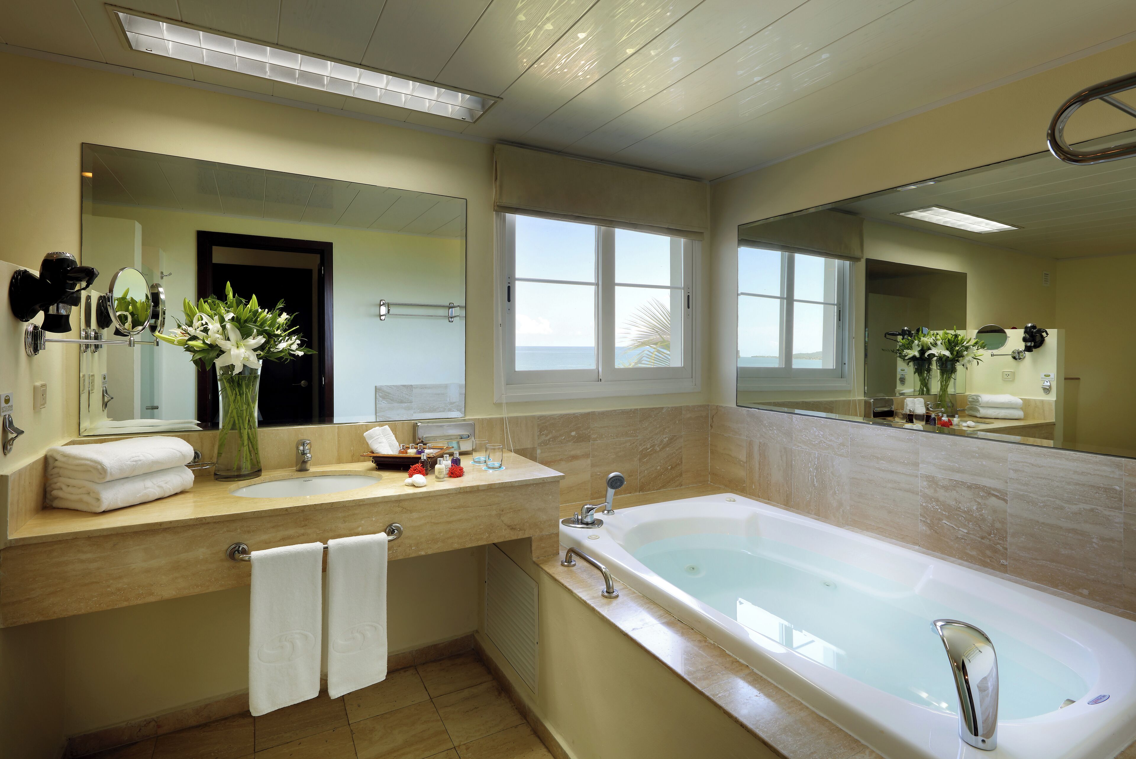 A modern bathroom with a large bathtub, a vanity with a mirror, and a window providing a view of the sea.