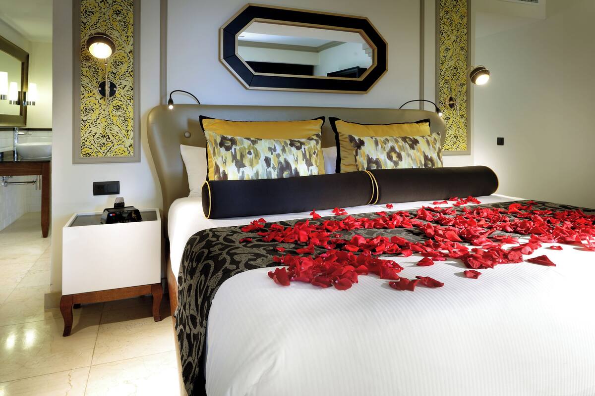 A hotel room with a large bed, a bedside table, a mirror, and a wall with decorative panels.