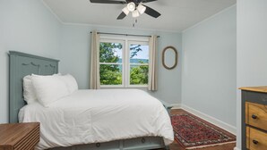Una camera da letto con un letto, una ventola a soffitto, una finestra con vista, un comò e un tappeto.