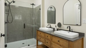 Un bagno moderno con doccia vetrata, due lavabi, uno specchio grande e mobili in legno.