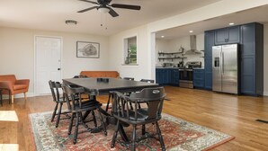 Un'ampia cucina con elettrodomestici moderni, una zona pranzo con un tavolo grande e sedie, e una ventola a soffitto.