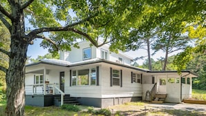 Een gelijkvloers huis met een veranda, een overdekt terras en een grote boom op de voorgrond.