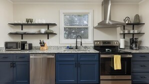 A modern kitchen with blue cabinets, stainless steel appliances, and a window with a view of trees. - The Meadow! Peaceful Getaway! (Chattanooga Valley)