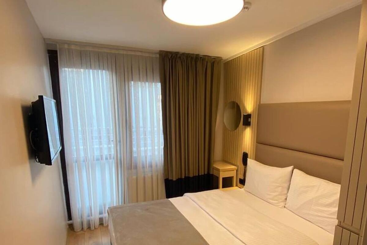 Una habitación de hotel con cama, televisión, lámpara de techo y cortinas.
