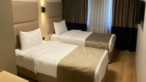 Una camera d'albergo con due letti, un tavolino, una lampada a soffitto e un televisore fissato al muro.