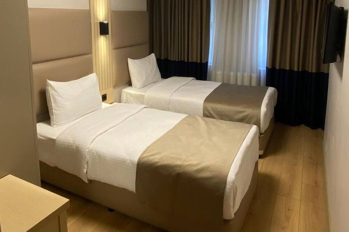Una habitación de hotel con dos camas, una mesita pequeña, una lámpara en el techo y un televisor colgado en la pared.