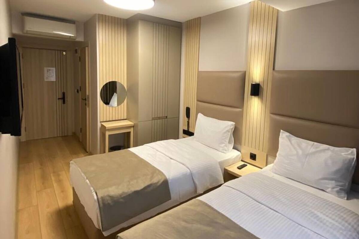 Habitación de hotel con dos camas, un espejo, mesitas de noche y una lámpara en el techo.