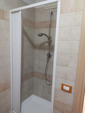 Una doccia con porta bianca, pareti piastrellate e soffione metallico.