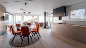 A modern kitchen with a large island, a dining area with orange chairs, and a view of the outdoors. - Runde Panorama - Eden (Heroy)
