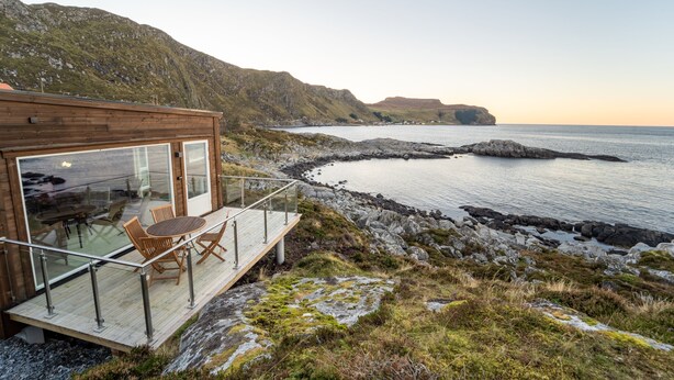 A wooden building with a glass balcony overlooking a rocky coastline and calm sea. - Runde Panorama - Eden (Heroy)