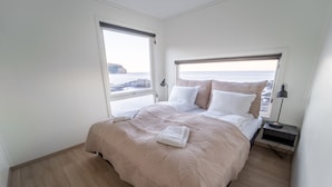 A bedroom with a large bed, a nightstand, and a window with a view of the sea. - Runde Panorama - Eden (Heroy)