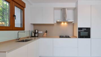 Una cocina moderna con armarios blancos, campana extractora de acero inoxidable, horno integrado y ventana con marco de madera.