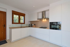 Una cocina moderna con gabinetes blancos, una campana de acero inoxidable, un horno empotrado y una ventana sobre el fregadero.