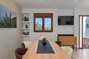 Un comedor moderno con una mesa de madera, sillas blancas, un posavasos negro y una planta en maceta.
