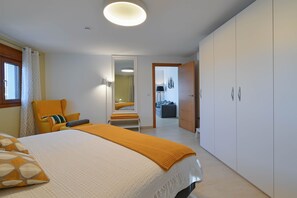 Un dormitorio con cama, una silla, un armario y una puerta que da a otra habitación.