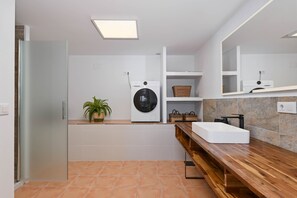 A modern bathroom with a built-in washing machine, a wooden vanity, and a large mirror.