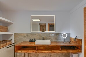 Un baño con un tocador de madera, un espejo grande y un espejo redondo.