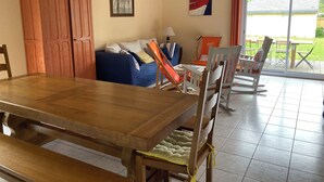 A dining area with a wooden table and benches, a blue sofa, and a view of the outdoors through a glass door. - Vacation home on enclosed land 800 metres from the beach and shops (Mesquer)