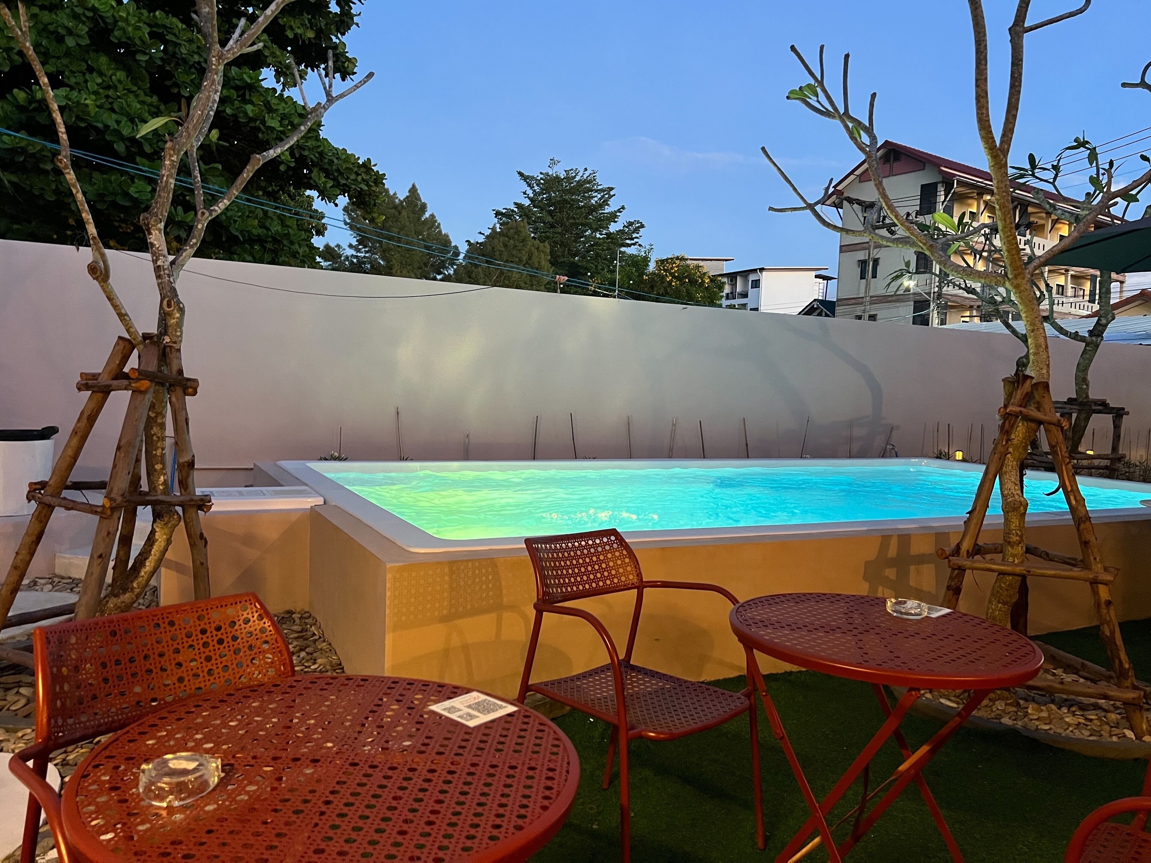 A pool area with a hot tub, surrounded by red metal chairs and tables, and a white wall in the background.