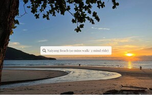 Cena de praia com pôr do sol, uma árvore e céu claro.