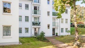 Un immeuble résidentiel à plusieurs étages, doté de balcons, d’une allée pavée et d’un petit jardin.