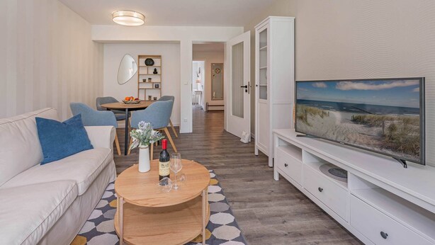 A modern living room with a sofa, a coffee table, a TV, and a dining area with chairs and a table. - Beautiful vacation apartment in Heringsdorf with terrace - only 400 m to the beach (Seebad Heringsdorf)