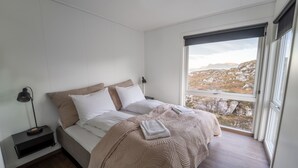Ein Schlafzimmer mit einem Bett, einem Nachttisch, einer Lampe und einem großen Fenster mit Blick auf felsiges Gelände.