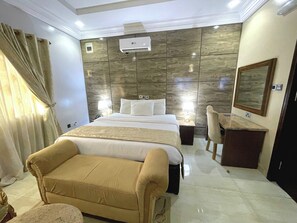 A hotel room with a large bed, bedside lamps, a vanity with a mirror, and a seating area with a chair. - Grand Bohabs Hotel (Abuja)