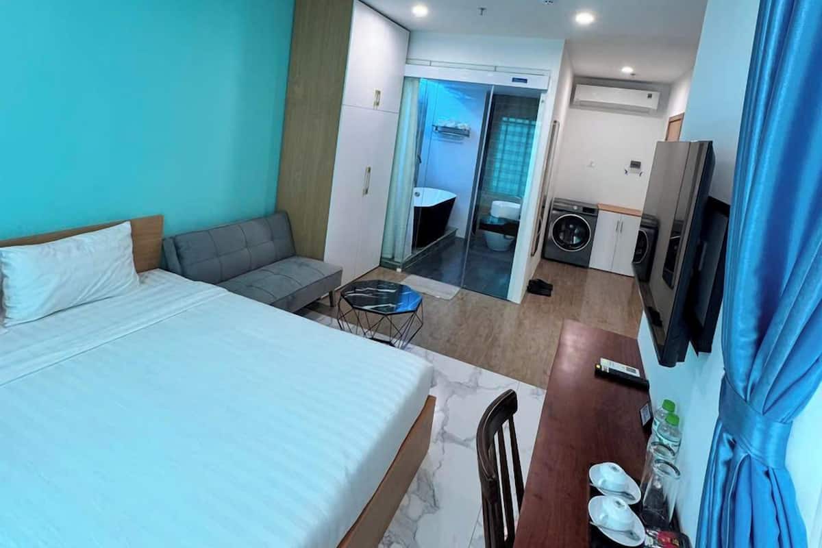 Ein Hotelzimmer mit Bett, einer Couch, einem kleinen Tisch, einem Fernseher und einem durchgegangenen Tür sichtbaren Badezimmer.