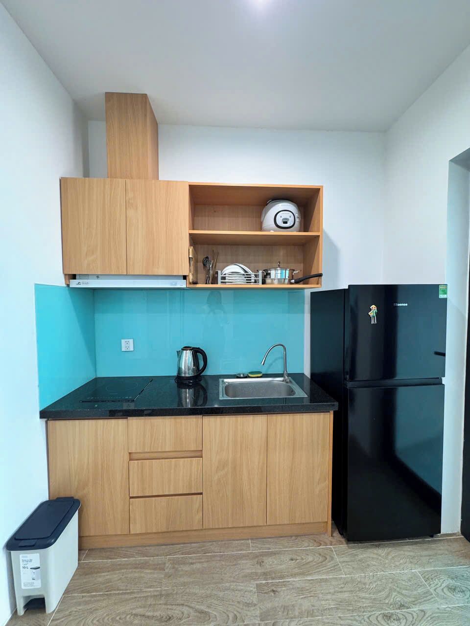 A compact kitchen with a black refrigerator, wooden cabinets, a sink, and a kettle.