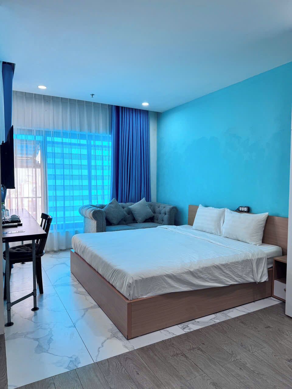 A modern hotel room with a large bed, a seating area with a sofa, and a dining table.
