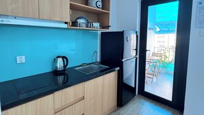 Una cocina moderna con armarios de madera, encimera negra, hervidor, pileta y refrigerador.