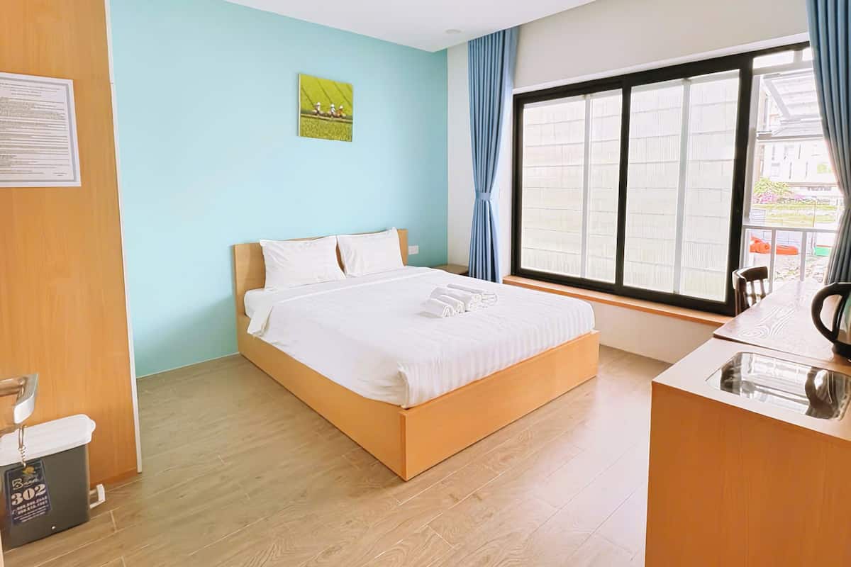 Ein Hotelzimmer mit Bett, Schreibtisch, Fenster mit Vorhängen und Holzboden.