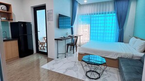 Una habitación moderna con cama, escritorio, silla, una mesita y una kitchenette.