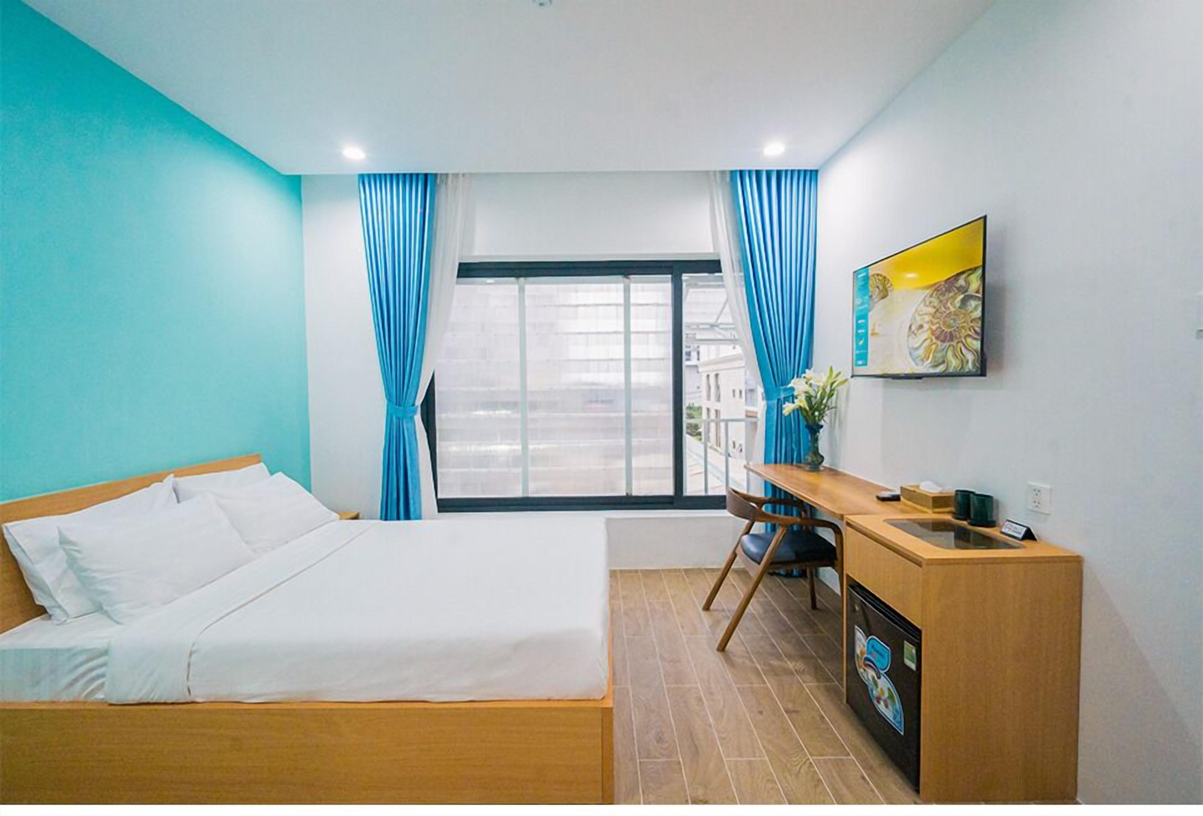 Une chambre d’hôtel avec un lit, un bureau, une chaise, une télévision et une fenêtre avec des rideaux.
