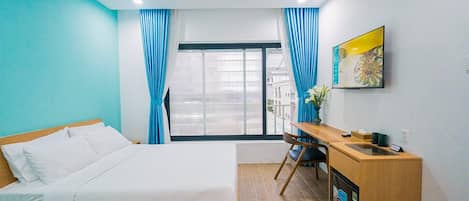 A hotel room with a bed, a desk, a chair, a TV, and a window with curtains.