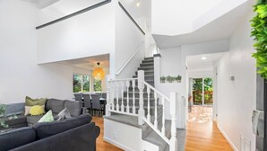 A modern living room with a grey sofa, a staircase with white balusters, and a dining area with a table and chairs. - Bodur's Rustling Leaves - EV Charge, BBQ, Privacy (Renton)