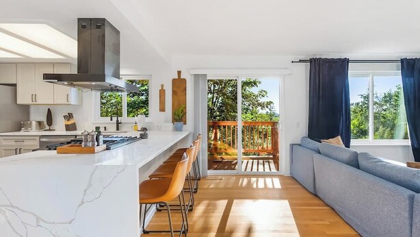A modern kitchen with a marble countertop, wooden bar stools, and a large island. - Bodur's Rustling Leaves - EV Charge, BBQ, Privacy (Renton)